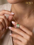 Gold necklace with a colorful pendant worn by a person, with 'ROKO' branding.