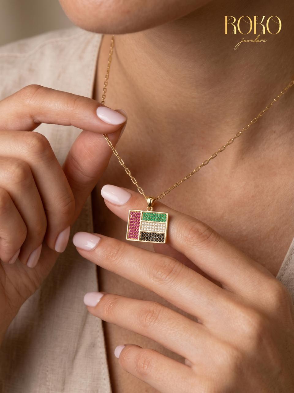 Gold necklace with a colorful pendant worn by a person, with 'ROKO' branding.