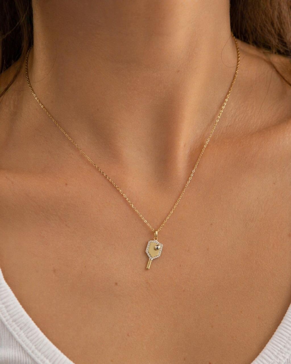 Gold necklace with a heart-shaped pendant on a person wearing a white top.