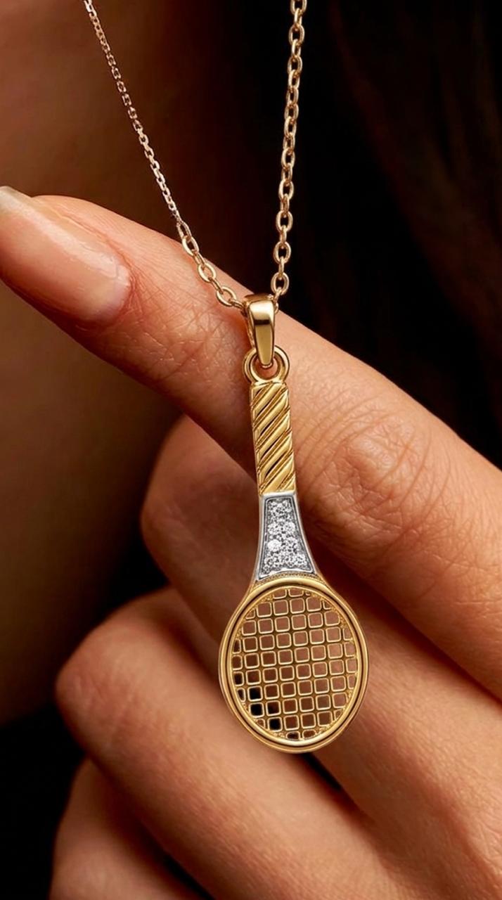 Gold tennis racket pendant on a chain held by a hand